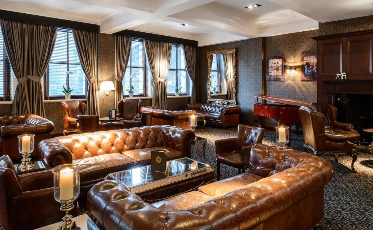 a living room with leather couches and a piano at The Vermont Hotel Newcastle in Newcastle upon Tyne
